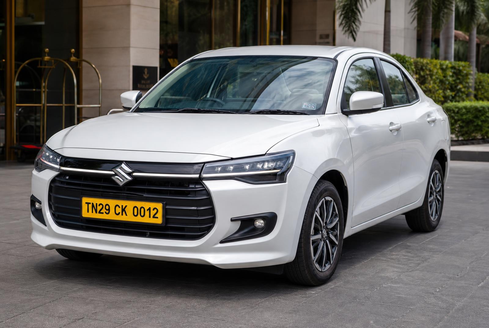 Maruti Suzuki Dzire · TN29 CK 0012 Front three-quarter of a pearl white Maruti Suzuki Dzire chauffeur taxi, yellow Tamil Nadu commercial number plate TN29 CK 0012, at a Tamil Nadu heritage hotel portico in Dharmapuri — POLAAMAA™ Executive Sedan